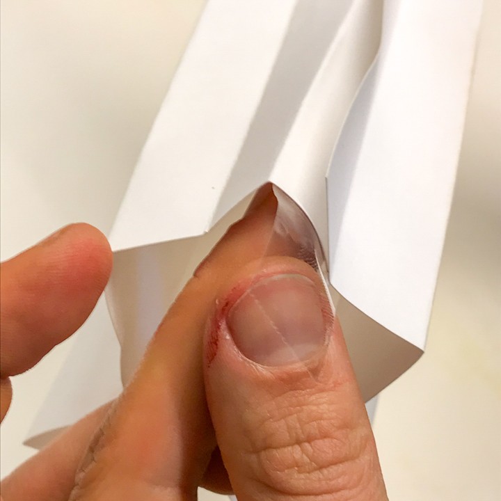 Das Foto zeigt eine weiße, zackige Röhre aus Papier. An den kurzen Seiten wird das Papier zusammengedrückt. Jemand befestigt ein Stück Klebeband dort.