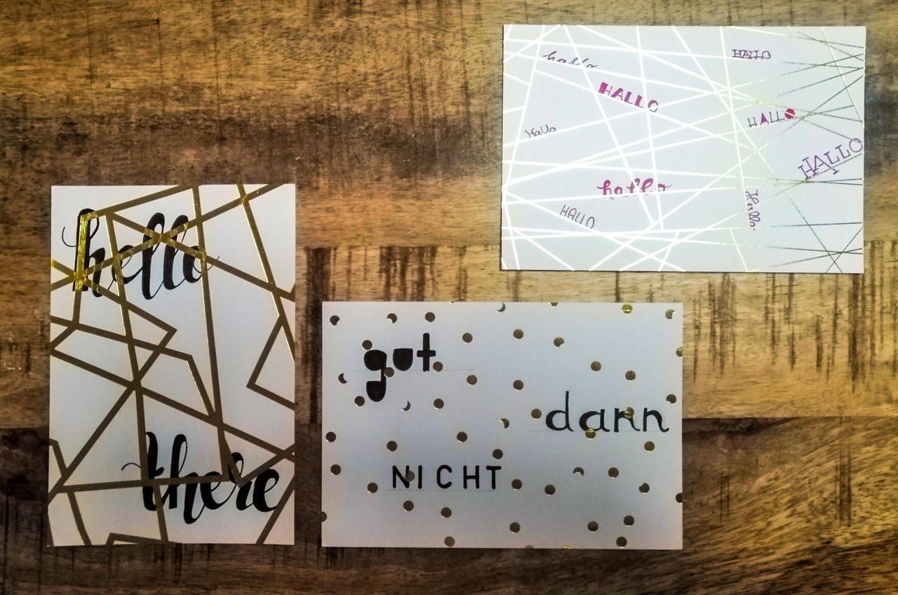 Das Foto zeigt verschiedene Handletterings im Postkartenformat. Ganz links liegt eine Karte mit dem Schriftzug „hello there“ in Schreibschrift. In der Mitte liegt eine weitere Karte mit den Worten „gut dann nicht“ in verschiedenen Schriftarten. Rechts oben liegt eine dritte Karte mit dem Wort „Hallo“. Es wurde mehrfach und in verschiedenen Schriftarten auf die Karte geschrieben.